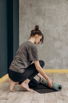 Young woman preparing yoga mat in a minimalist room for an indoor workout session.