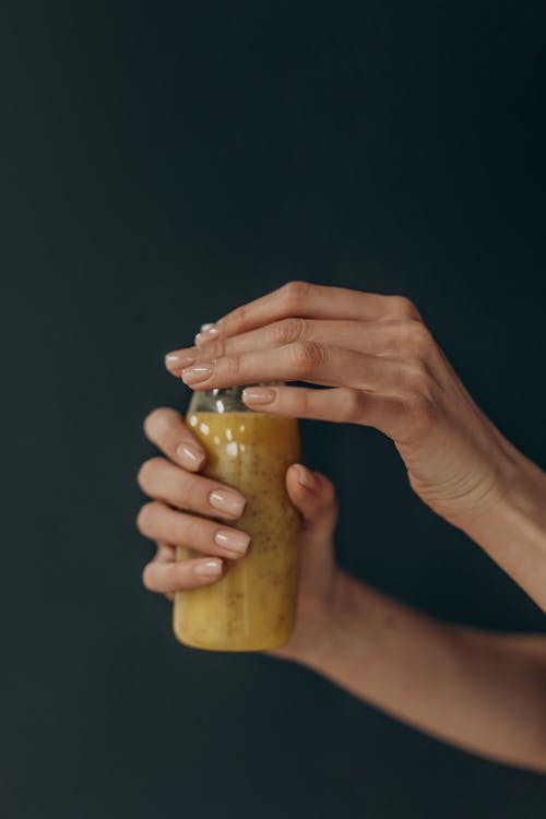 Person Holding Clear Glass Jar With Yellow Liquid