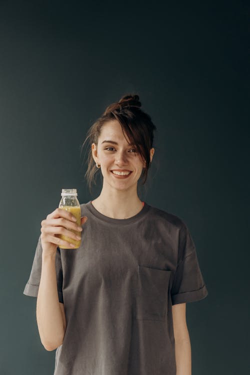 Smiling Woman in Black Crew Neck T-shirt Holding Clear Glass Bottle