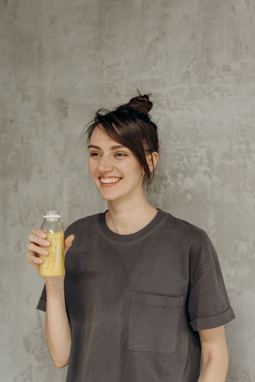 Free Smiling young woman in casual wear holding a bottle of healthy juice indoors. Stock Photo