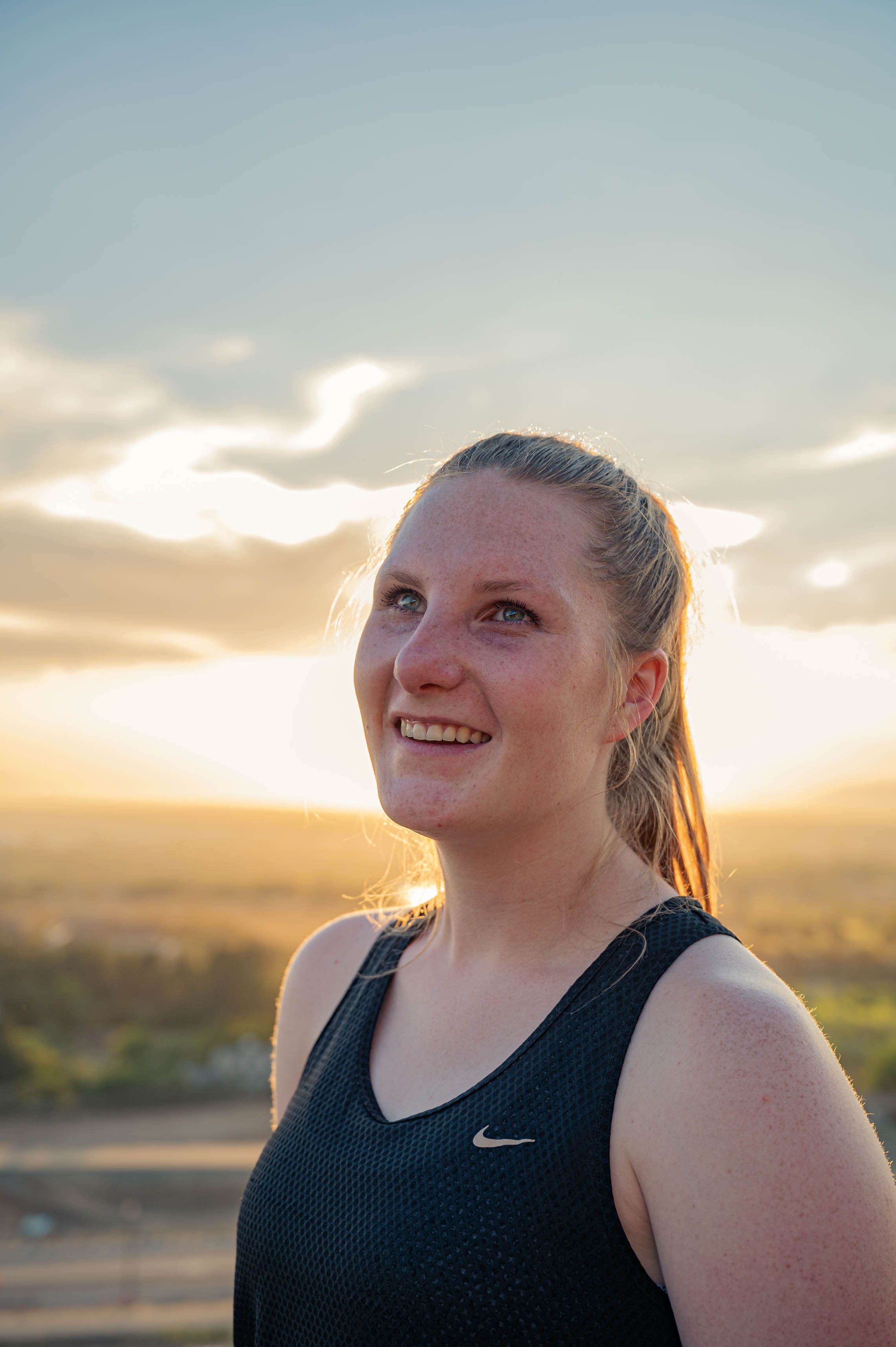 Portrait of a young woman in a tank top smiling at sunset outdoors, capturing a joyful summer moment.