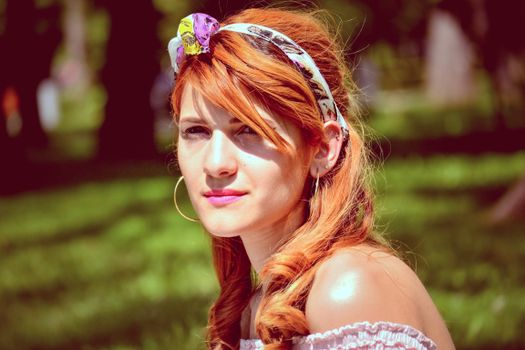 Portrait of a young woman with red hair and headband, enjoying a sunny day in the park.