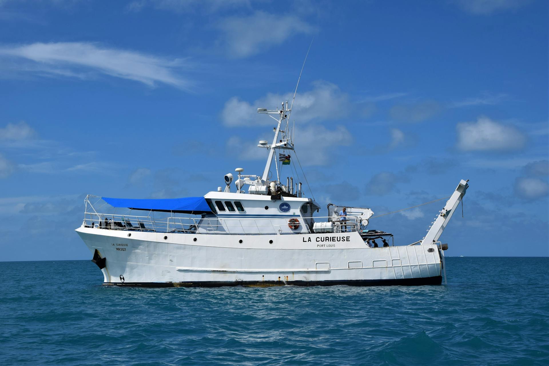 A research vessel named La Curieuse sails on calm blue ocean under clear skies.