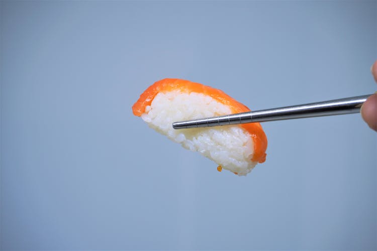 Person Using A Metal Chopstick On Salmon Sushi 