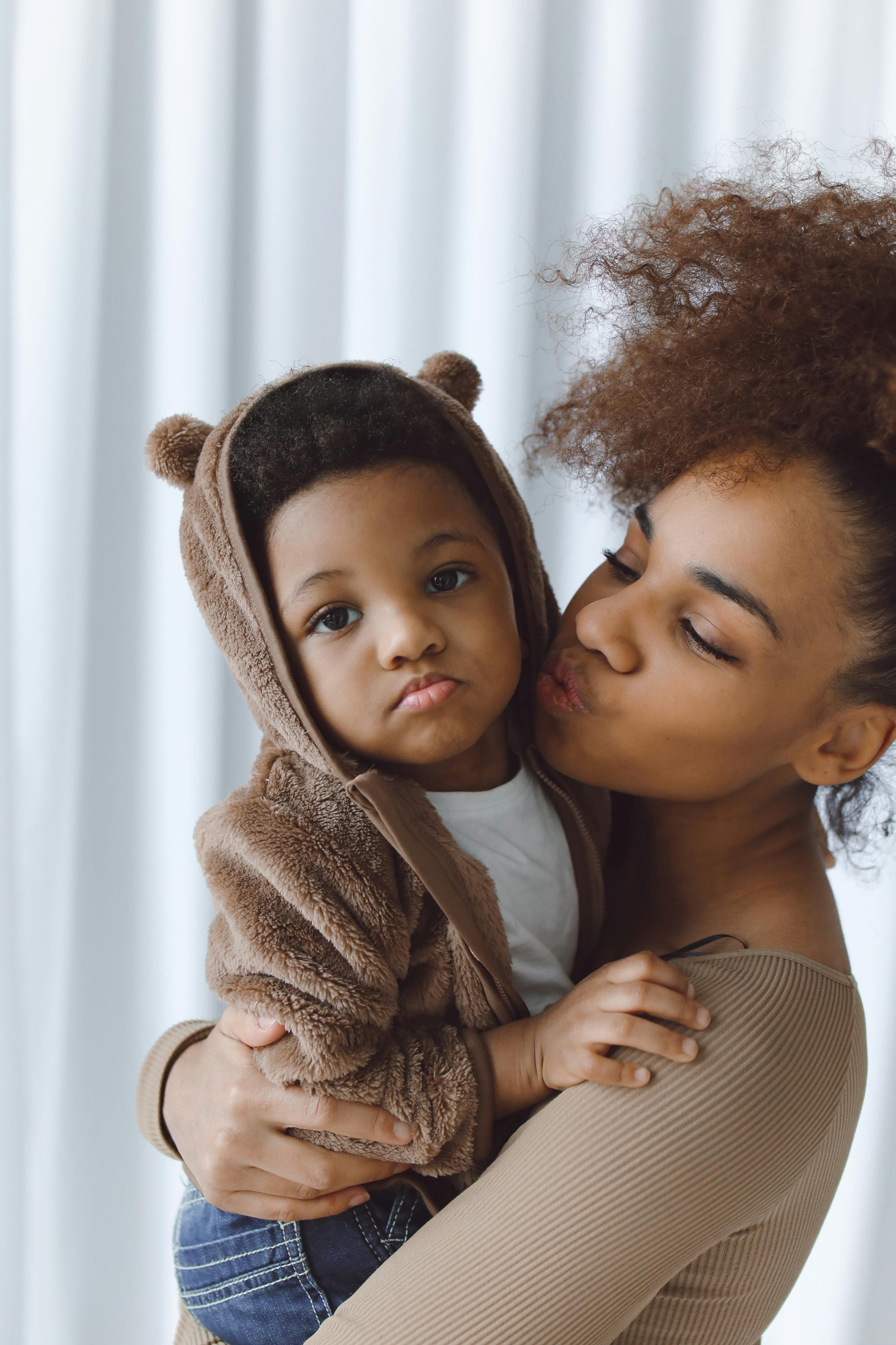 photo of a mother kissing her cute kid looking at the camera