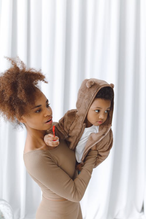 Woman in Beige Long Sleeve Dress Carrying a Boy In Brown Hoodie