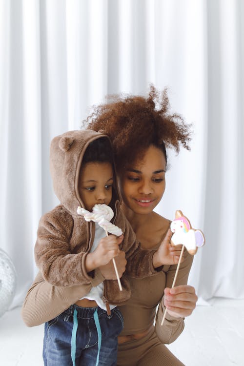 Woman Cuddling a Boy Eating Marshmallow Candy on Stick