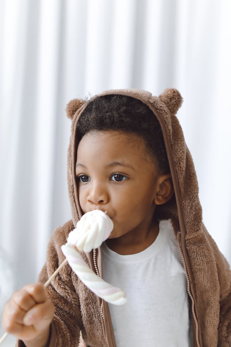 Boy In Brown Hoodie Jacket Eating Marshmallow Candy On Stick