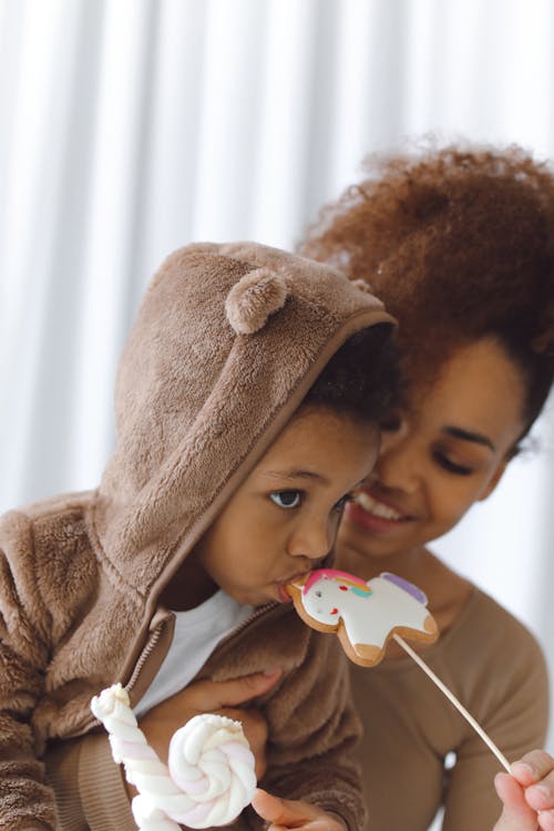 Free Woman Holding a Boy Eating a Candy Cookie on Stick Stock Photo