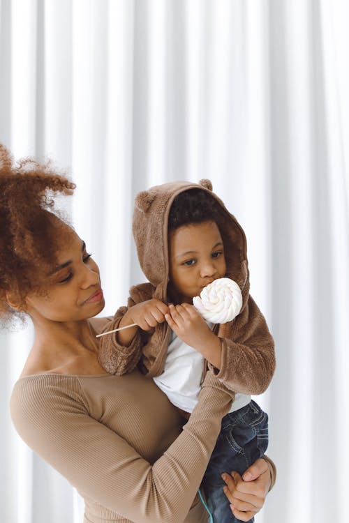 Free Woman Carrying a Boy Eating Marshmallow Candy Stock Photo