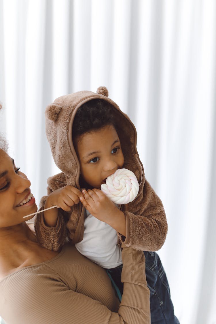 Smiling Woman Carrying A Boy Eating Marshmallow Candy