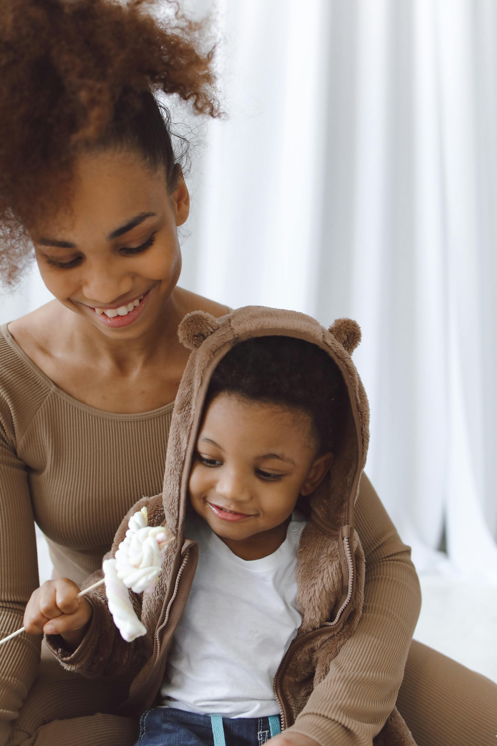 a child in brown hoodie sitting on a woman s lap smiling