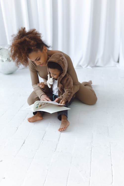 Free Woman Reading a Book With Child Holding a Lollipop Stock Photo