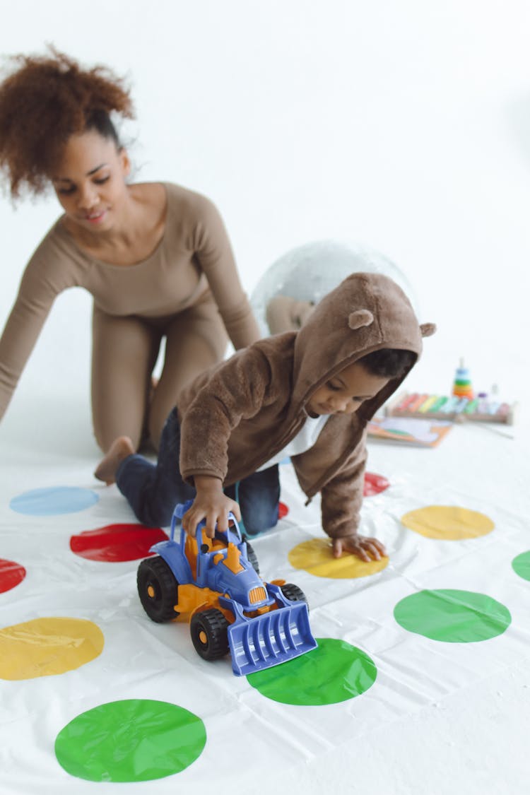 A Woman And A Child Playing With Toy Truck On A Polka Dot Mat