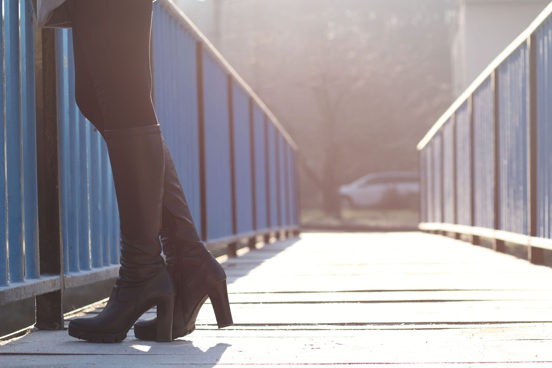 Close-up of a woman's black boots on a sunny urban bridge, capturing a modern city vibe.