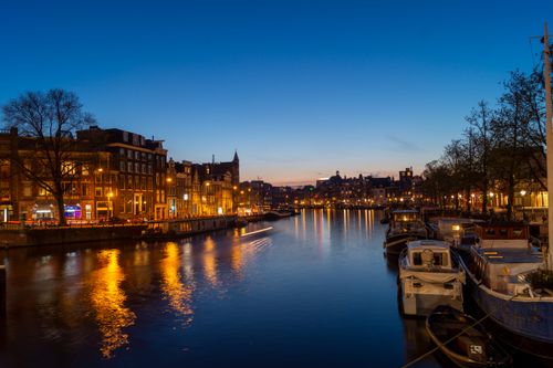 Free Stunning view of Amsterdam's lit-up canal and cityscape at twilight, reflecting off the water. Stock Photo