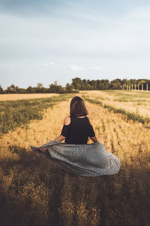 Faceless lady admiring rural fields against cloudy sky