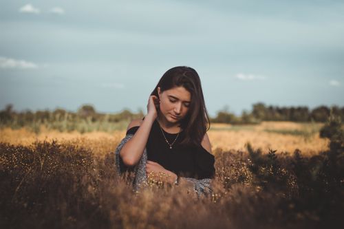 Free Pensive young female in casual clothes and bare shoulders standing in field with dry grass and looking down in autumn Stock Photo