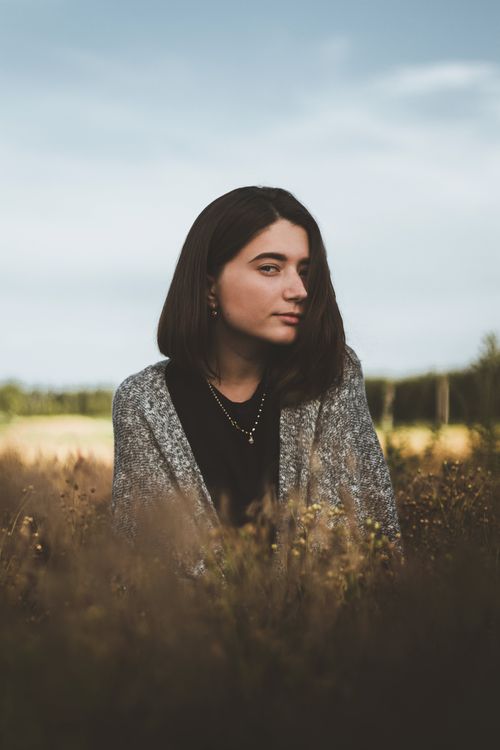Free Young female with dark hair in casual clothes looking at camera while standing in meadow in countryside in autumn Stock Photo