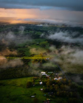 Stunning aerial view capturing lush farmland and misty clouds at sunset, showcasing nature's beauty.