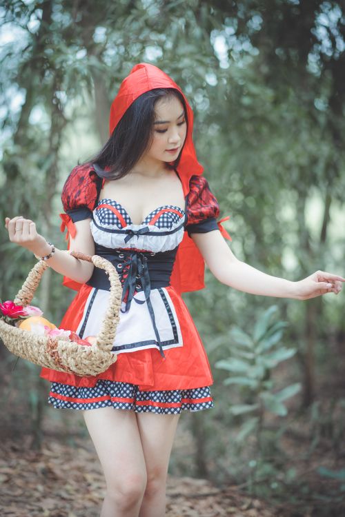 Free Charming portrait of a woman dressed as Little Red Riding Hood in a forest setting, carrying a basket. Stock Photo