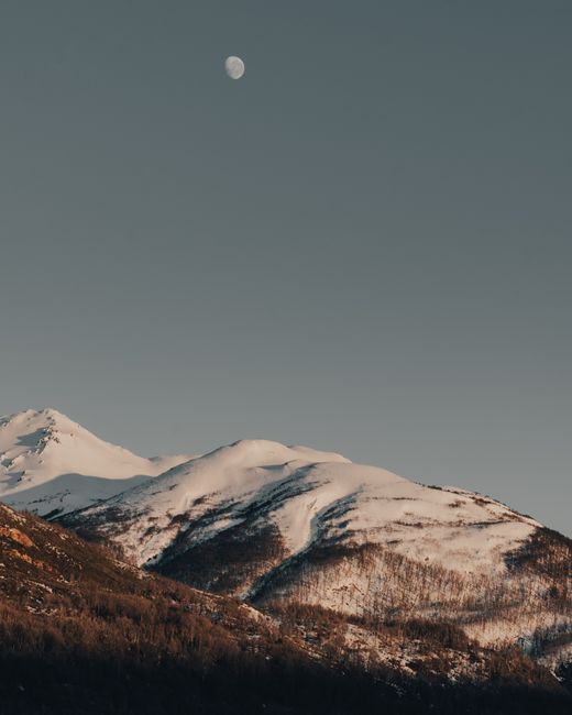 A tranquil mountain scene with snow-covered peaks and a clear, moonlit sky.