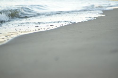 Free A calming image of gentle waves washing onto a sandy beach under soft daylight. Stock Photo