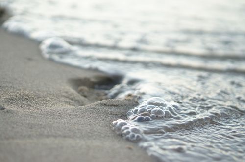 Free Gentle waves lapping on the sandy shore create mesmerizing bubbles, capturing the calm essence of the beach. Stock Photo