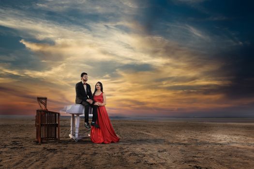 Beautiful couple in formal attire at a beach during sunset with a piano. - Fotografer Sidoarjo
