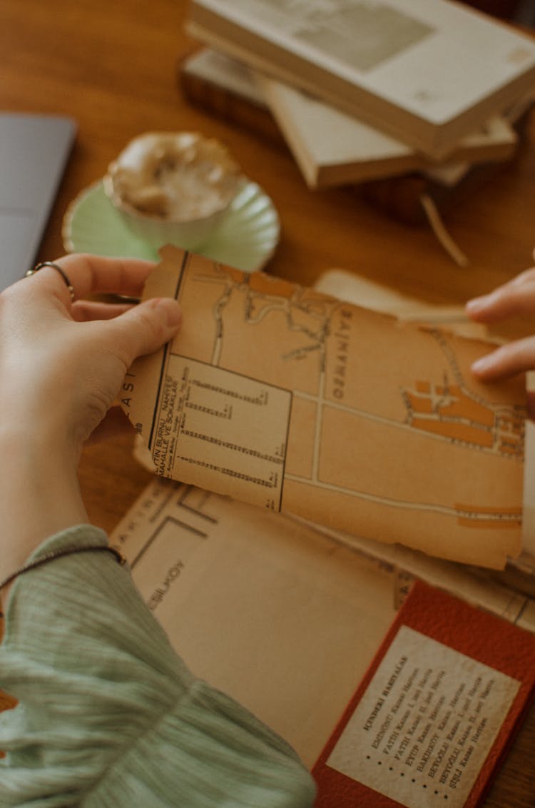 Faceless Female Looking Through Old Maps At Table Near Books