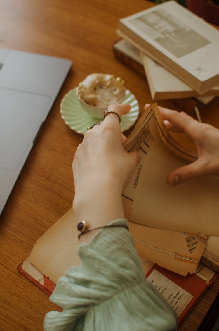 Unrecognizable Woman Examining Documents At Table Near Laptop And Books