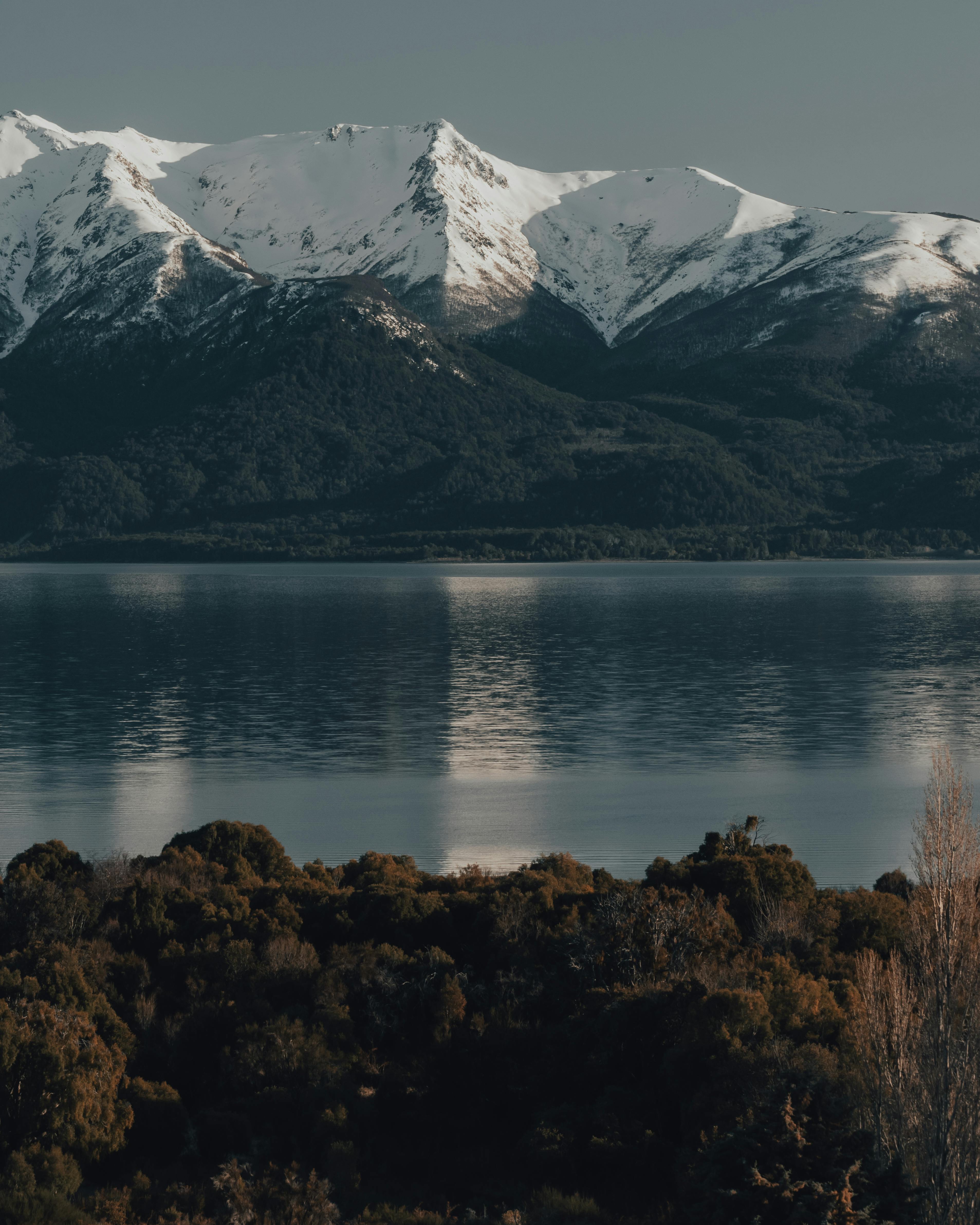 Stunning view of snow-covered mountain range reflecting in a tranquil lake with lush green foreground.