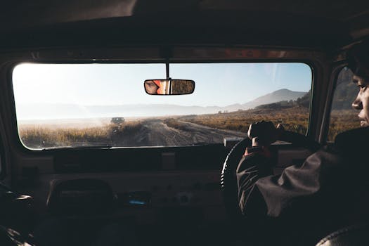 Interior view of a car driving along a dirt road with a scenic countryside landscape visible through the windshield.