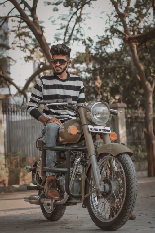 Free Young man with sunglasses and striped sweatshirt sitting on a vintage motorcycle outdoors. Stock Photo