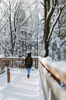 A woman walks along a snow-covered wooden path surrounded by winter trees.
