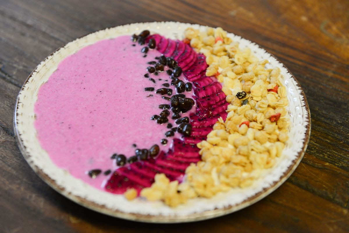 Bright pink pitaya smoothie bowl with dragon fruit slices, cacao nibs and crunchy granola