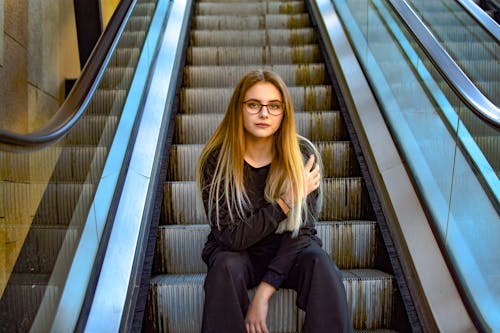 Free Woman Wearing Eyeglasses Sitting on Escalator Stock Photo