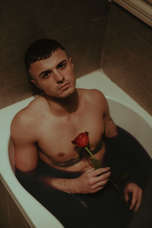 Free A contemplative man holding a rose submerged in a bathtub, creating a serene and moody atmosphere. Stock Photo