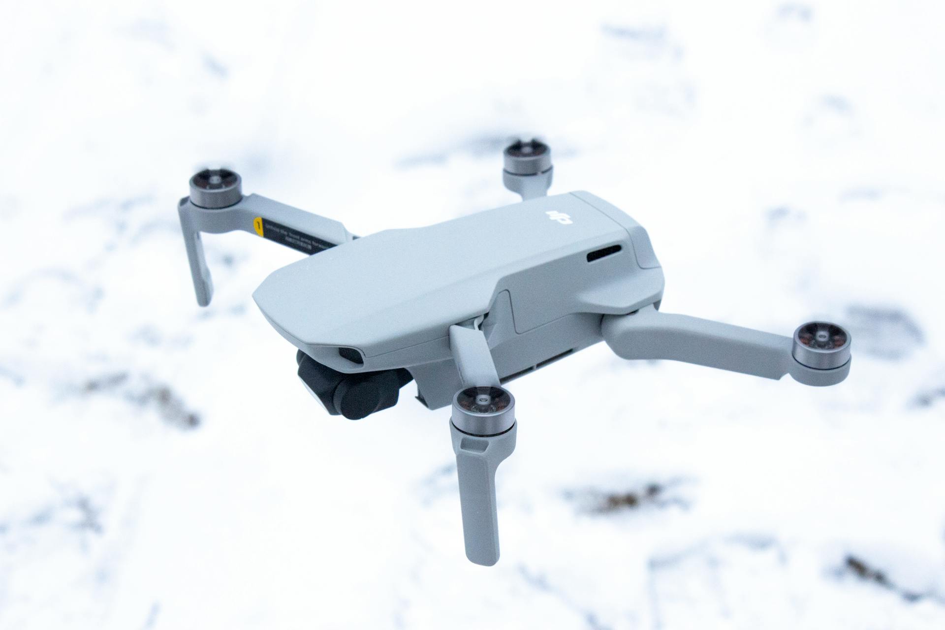 A compact drone in flight over a snowy landscape, showcasing its sleek design.