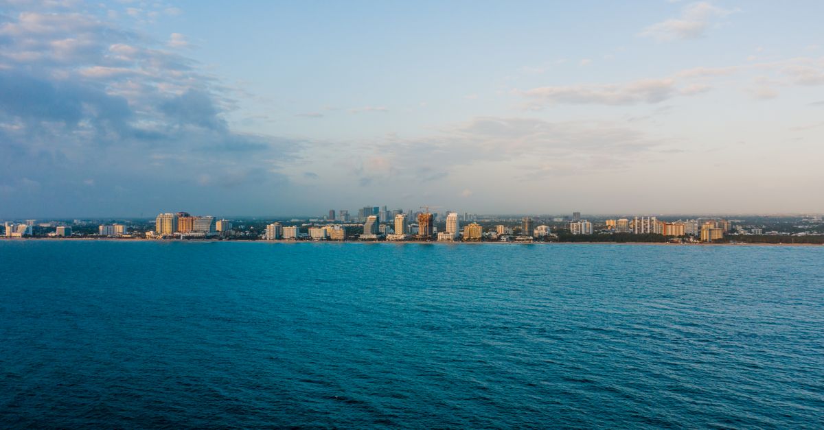 Picturesque scenery of modern city skyline with multistory buildings located near rippling blue sea under cloudy sunset sky
