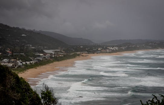 Dramatic scenic view of a coastal town, beach, and waves under cloudy skies.