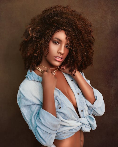 Young African American female with Afro hairstyle wearing tied shirt on bare body touching necklace and looking at camera