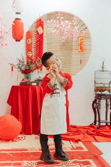 Young Asian child in traditional attire celebrating Chinese New Year indoors with decorations.