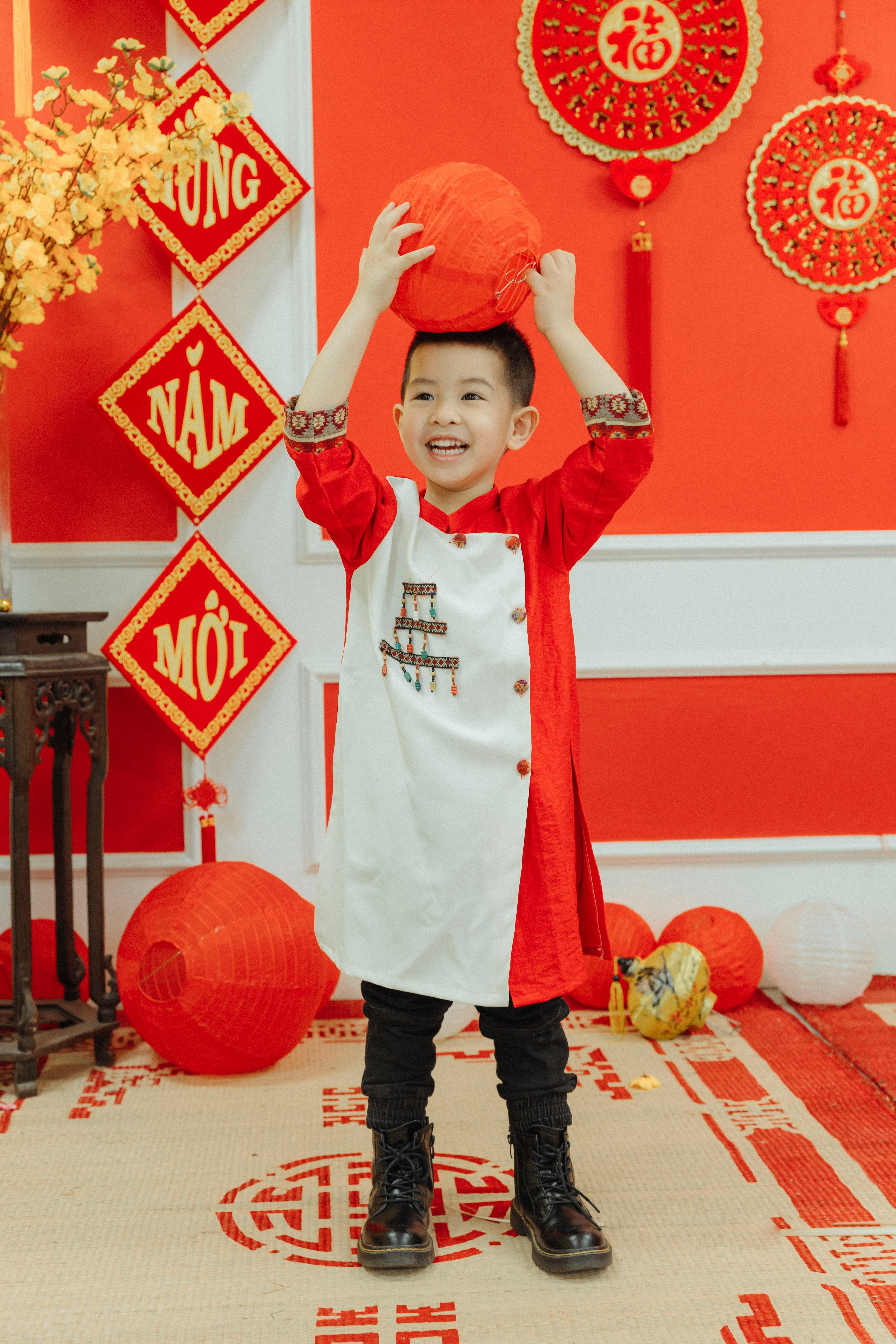 A joyful child wearing ao dai holds a red lantern, surrounded by festive decorations.
