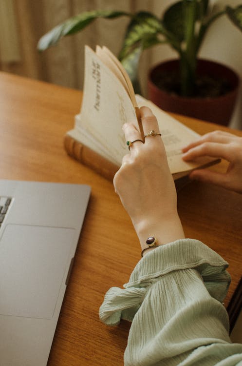 Free Unrecognizable woman reading book at table near laptop Stock Photo