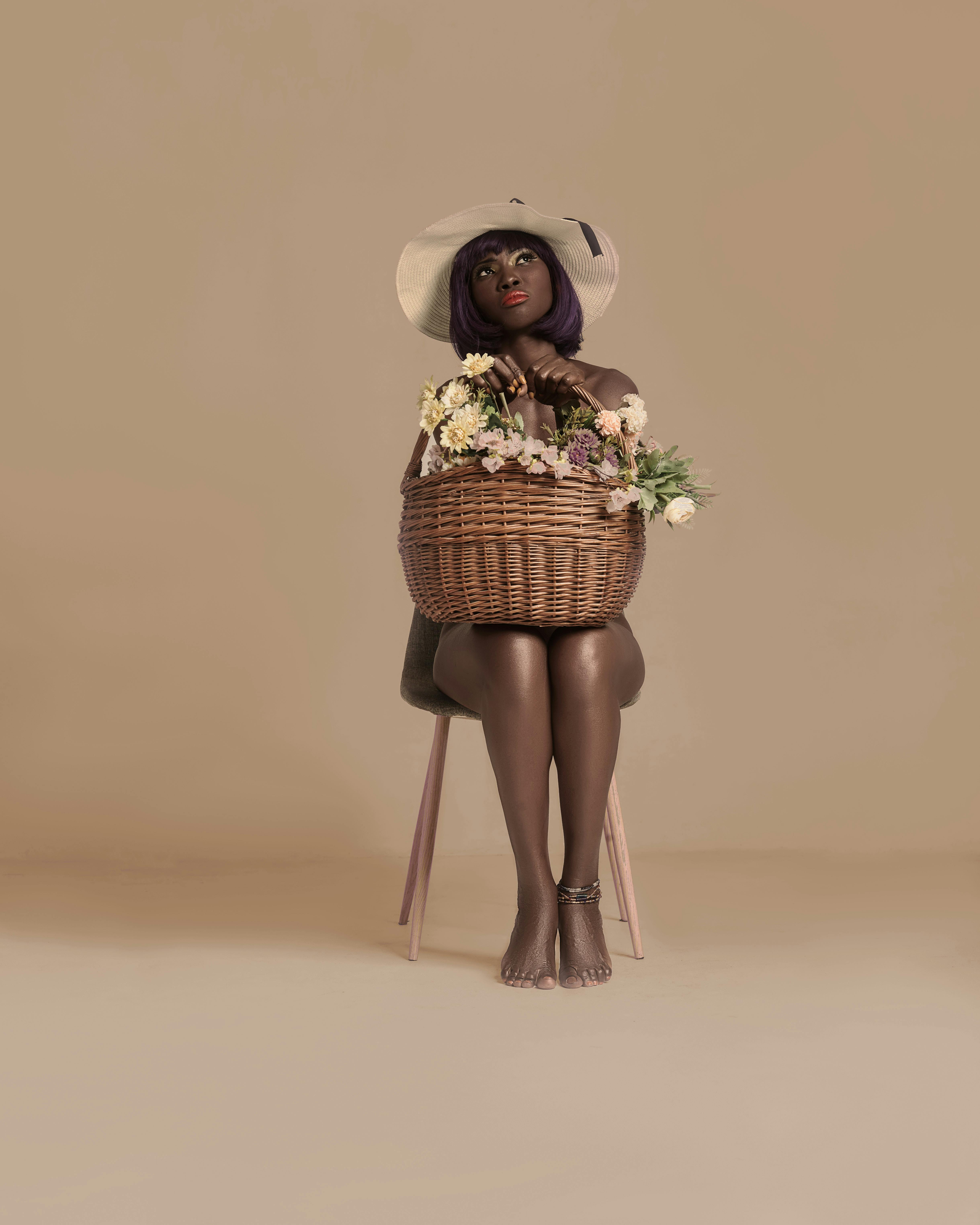 Fashionable woman with purple hair sitting with a woven basket against a beige background.
