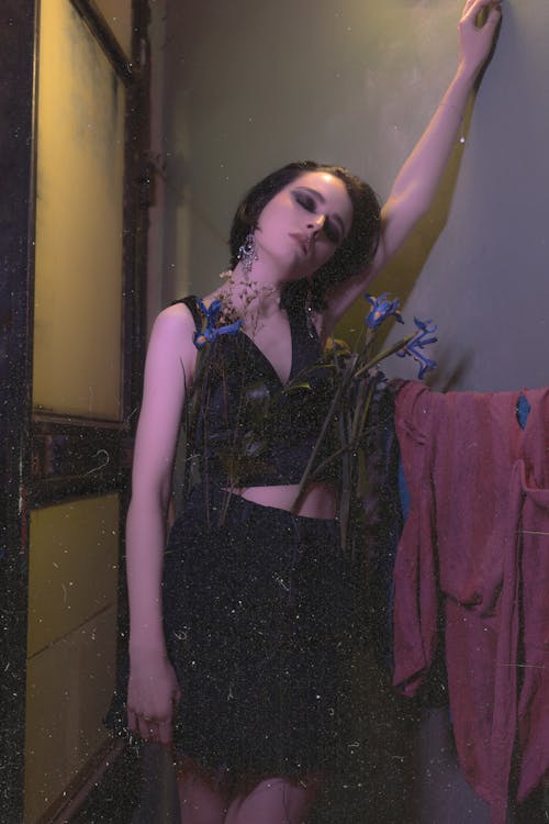 Extravagant female with dark hair and eyes closed in dark apartment with blooming blue flowers