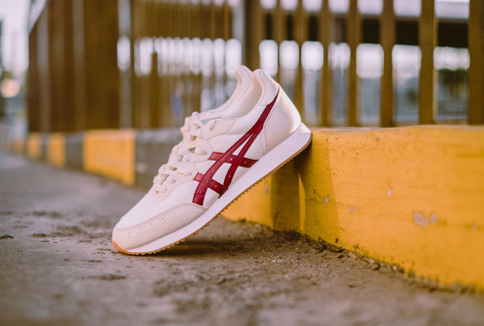 Close-up of a stylish white sneaker with red accents leaning against a yellow curb in an urban setting.