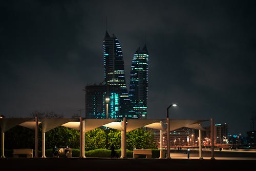 Park with Illuminated Canopy Near the High Rise Building During Night Time