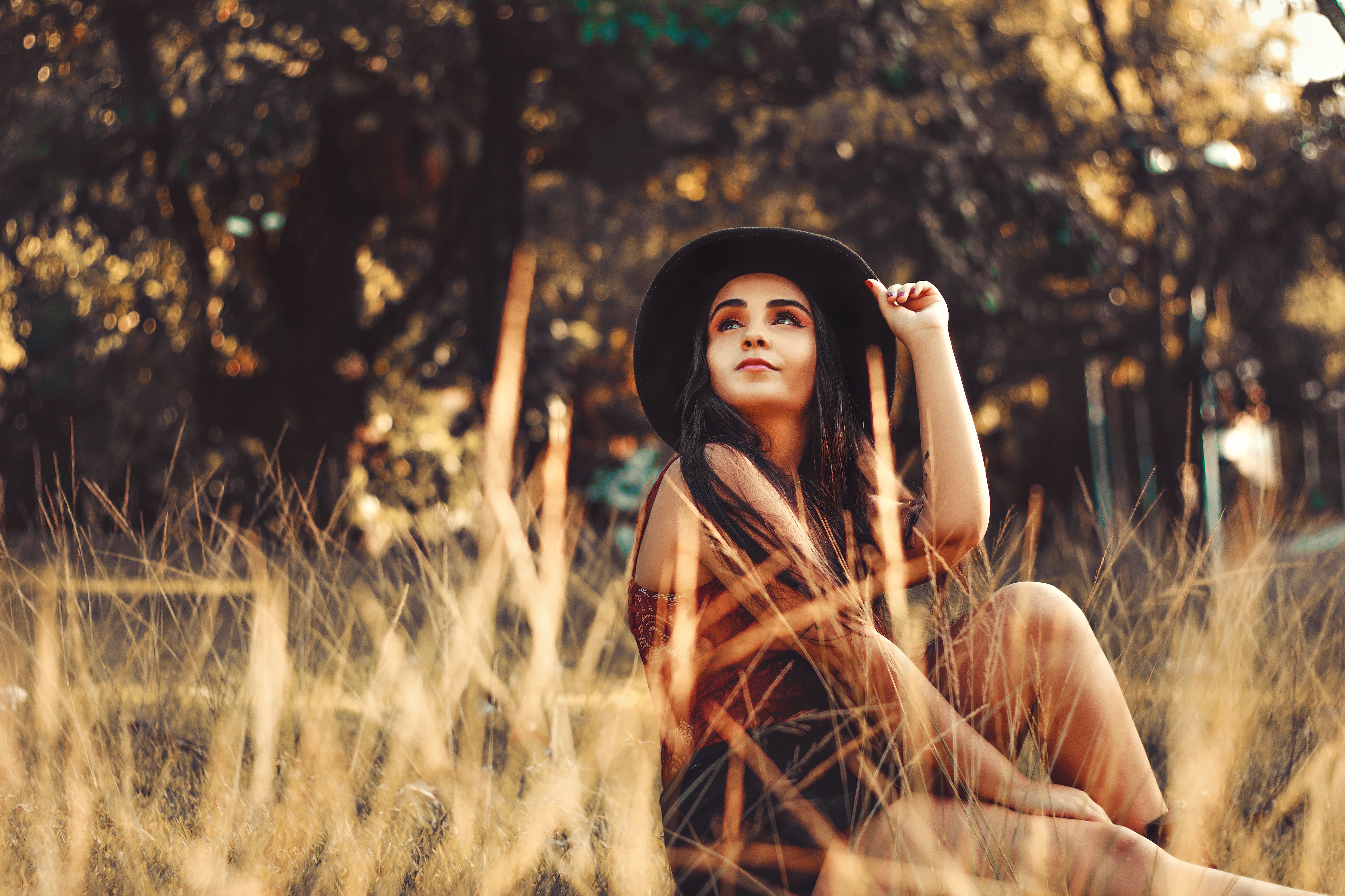 Young woman wearing a hat sitting in a grassy field, enjoying the autumn scenery.